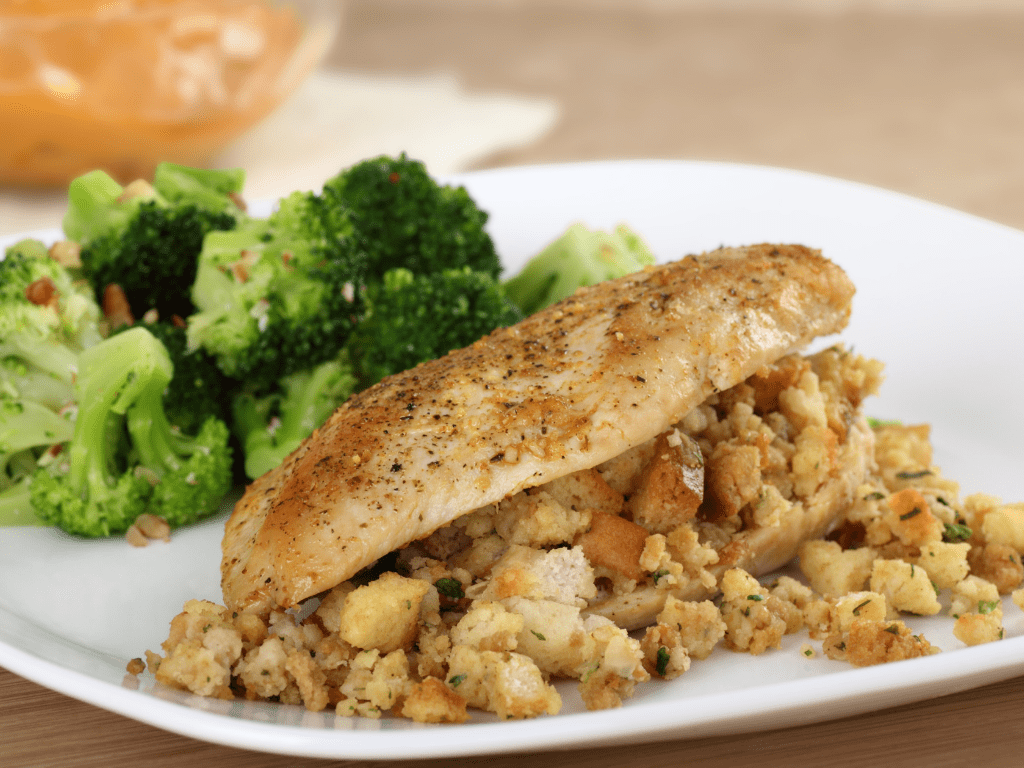 A white dinner plate with a chicken breast, stuffing and broccoli.