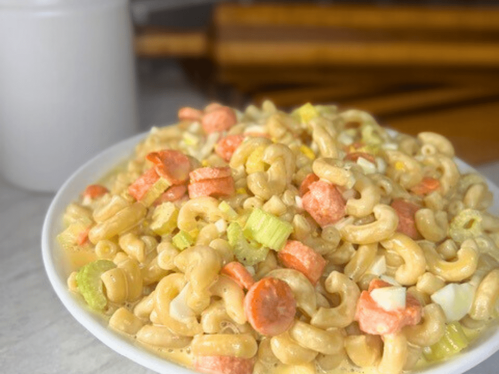 Creamy macaroni salad in a white bowl sitting on the kitchen counter.