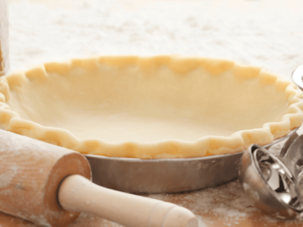 Pie crust sitting next to a rolling pin on a floury surface