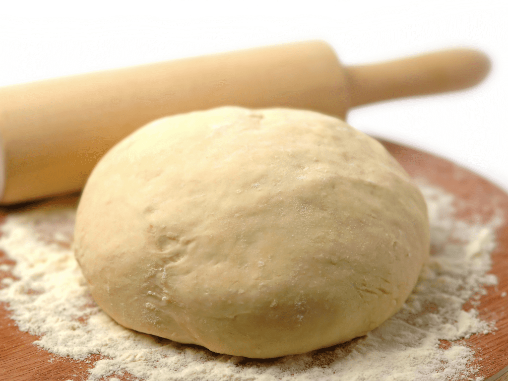 homemade pizza dough ball resting on a cutting board before rising