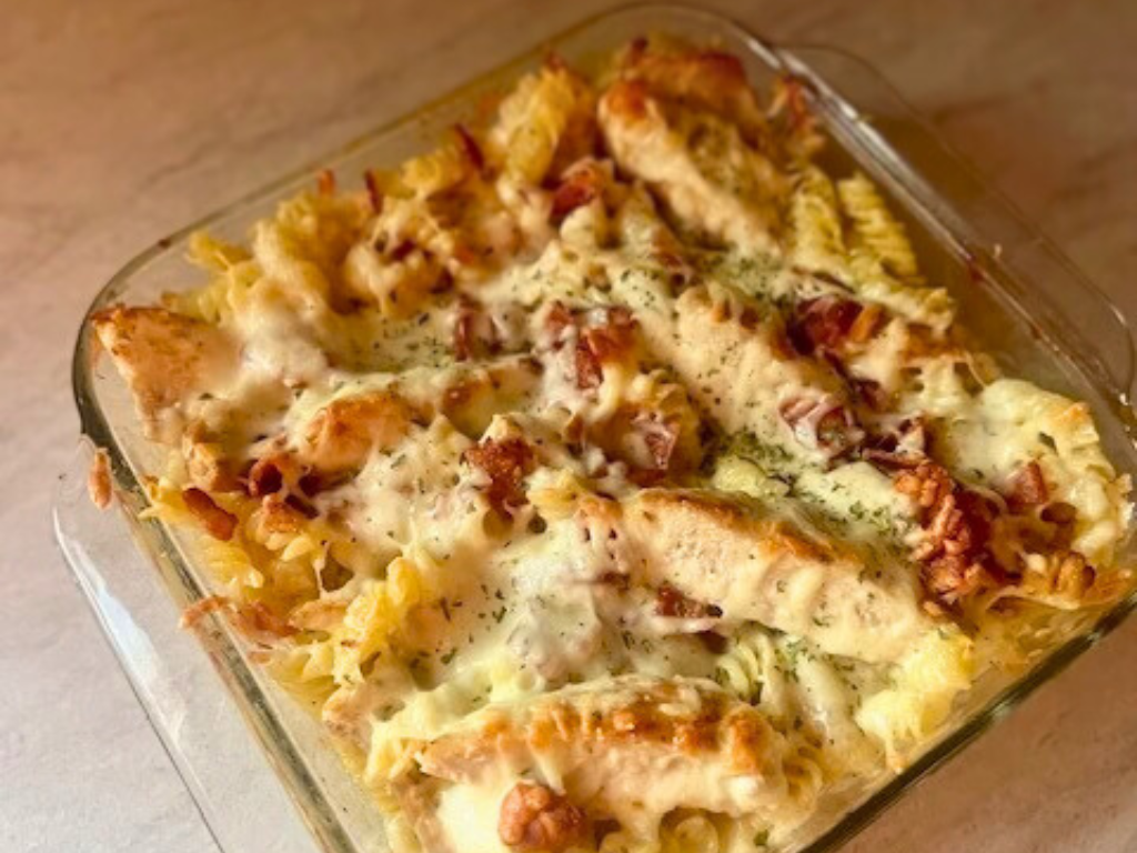 Creamy three cheese chicken pasta casserole with bacon and parsley baked in clear dish