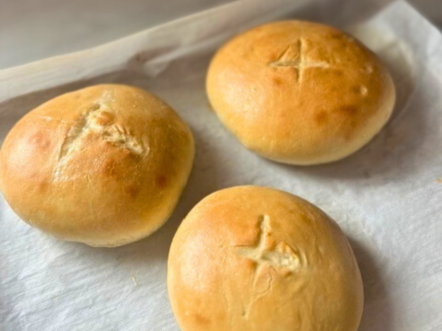 Baked bread bowl rounds scored with an X on a baking sheet