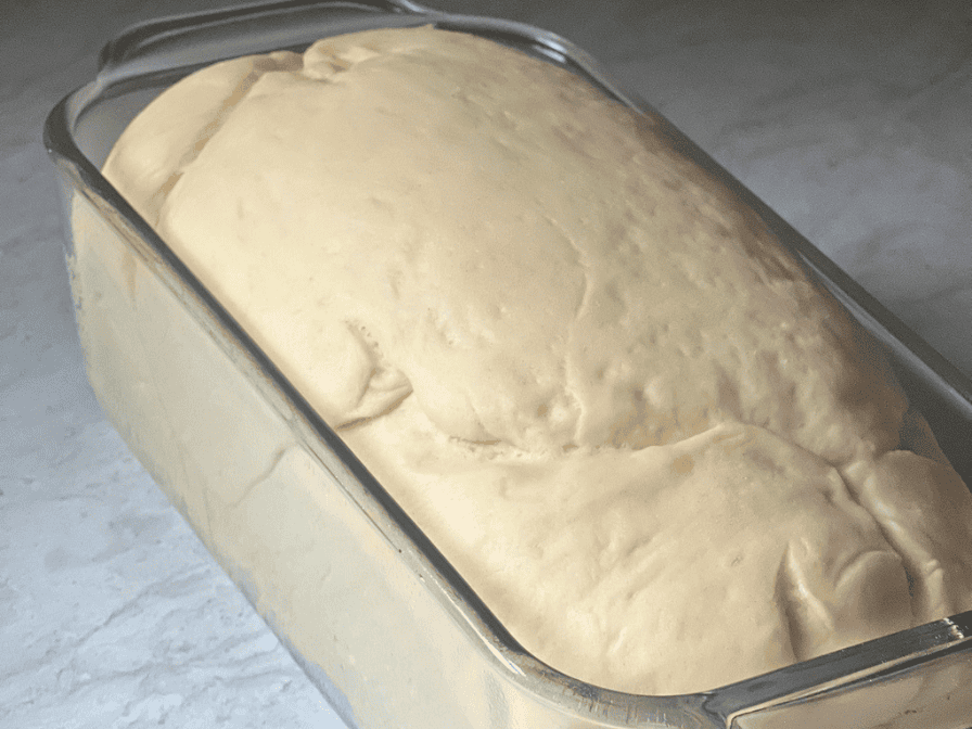 Soft homemade bread dough rising in a loaf pan before baking, showing a well-proofed dough