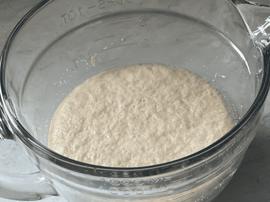 Yeast blooming in warm water and sugar in a bowl, forming a foamy layer for homemade bread