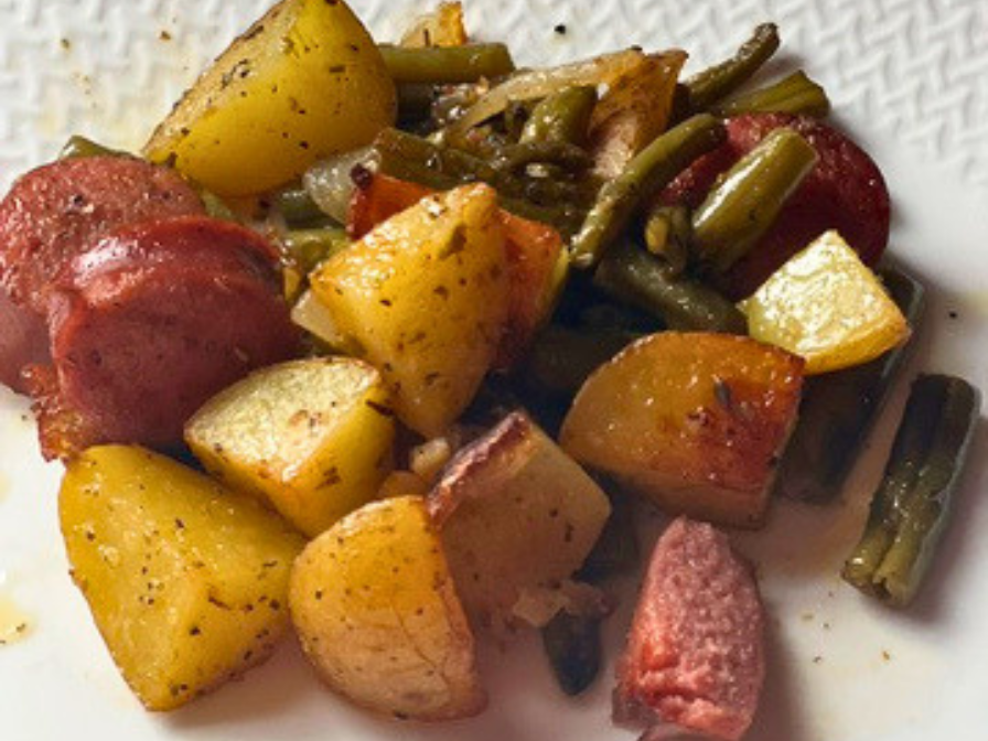 Sheet pan dinner with sliced kielbasa, roasted potatoes, and green beans with visible herbs and melted butte