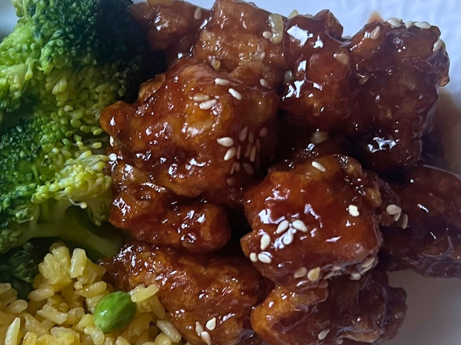 Crispy homemade sesame chicken coated in a glossy sauce topped with sesame seeds and green onions