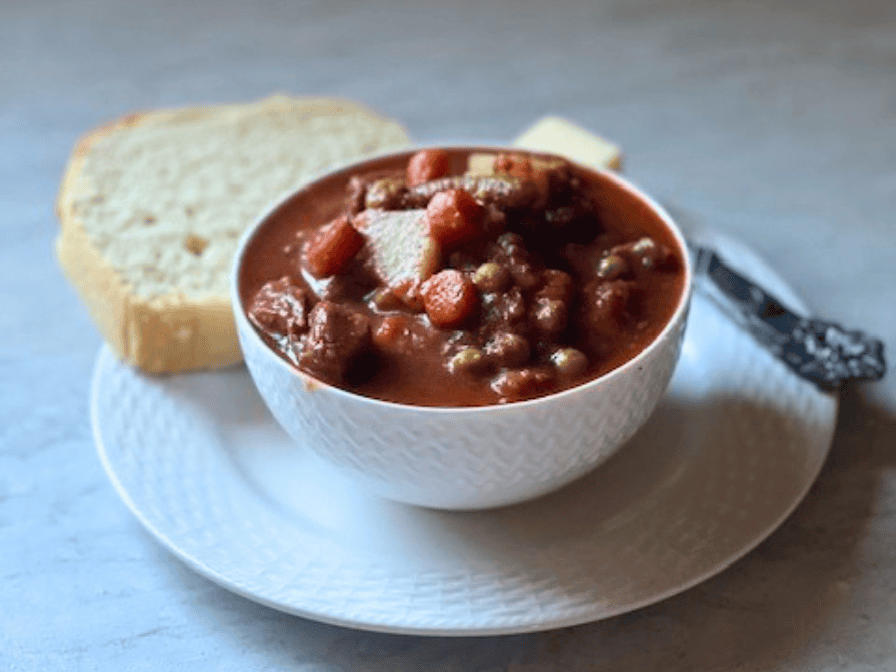 A bowl of hearty vegetable beef soup with tender chunks of beef, potatoes, carrots, and green beans in a rich tomato broth