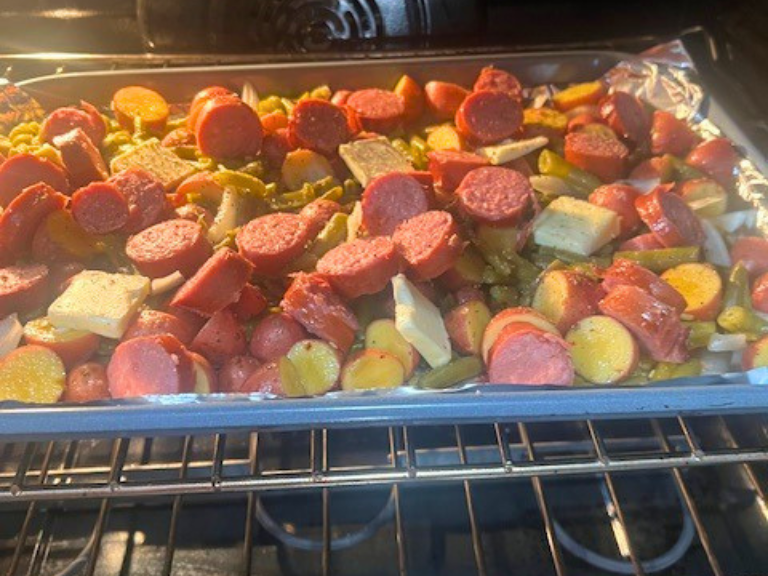 Sheet pan kielbasa potatoes and green beans in the oven with pats of butter melting on top