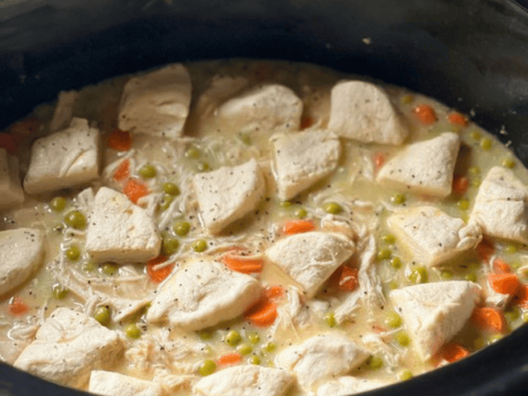 Biscuit dough pieces placed on top of chicken and vegetable mixture in a slow cooker before cooking.