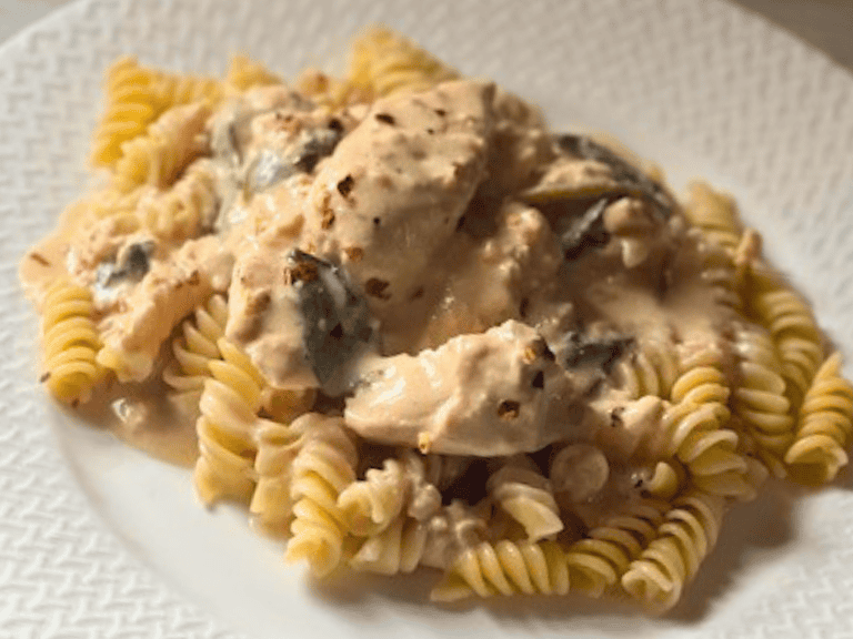 Creamy crockpot Italian chicken served over noodles on a white plate with Parmesan cheese and parsley garnish.
