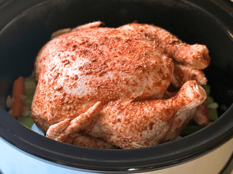 Whole seasoned chicken cooking in a slow cooker over carrots, celery, onion, and garlic.