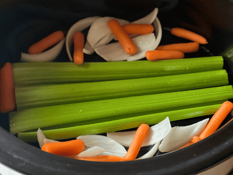 Slow cooker lined with celery stalks to create a rack for cooking a whole chicken.