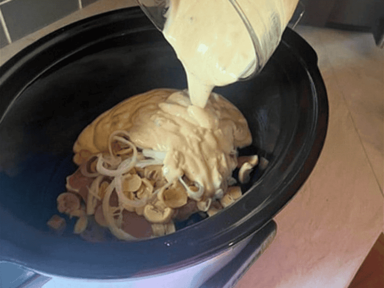 Pouring creamy mushroom gravy mixture over pork chops with mushrooms and onions in a slow cooker