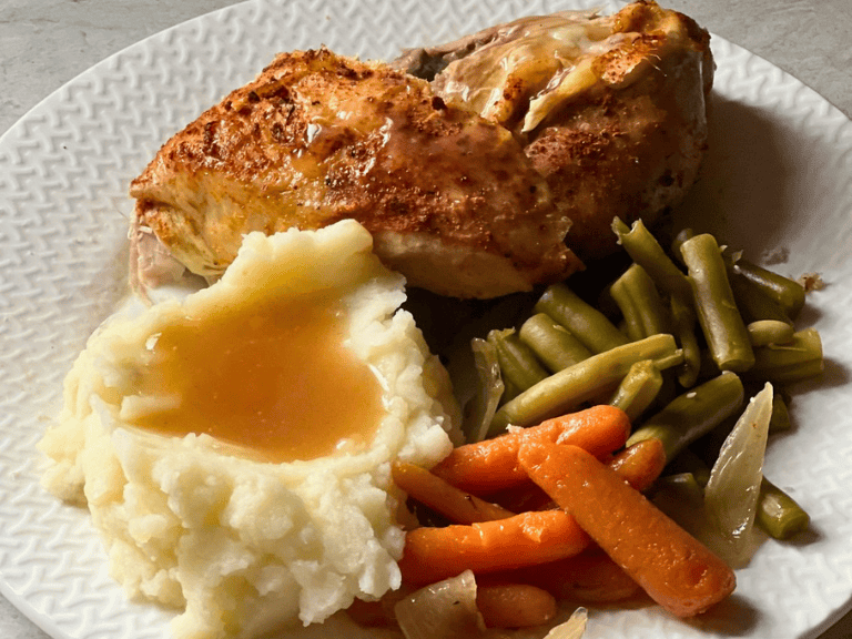 Slow cooker chicken breast served with mashed potatoes, gravy, and cooked carrots on a dinner plate.