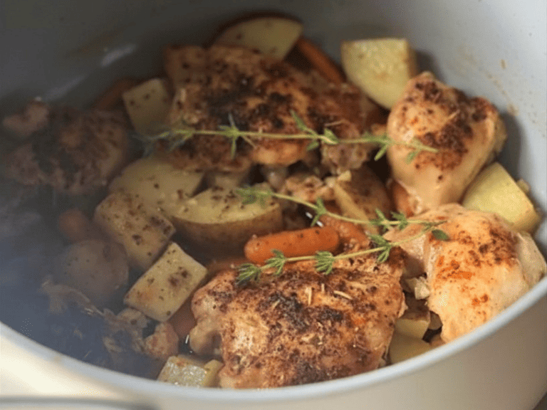 Golden brown chicken thighs cooking in a Dutch oven with lemon slices, garlic, and savory broth.