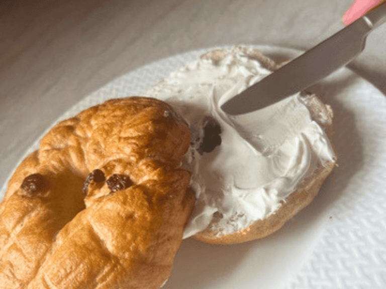 Person spreading cream cheese onto a homemade cinnamon raisin sourdough discard bagel with a butter knife.