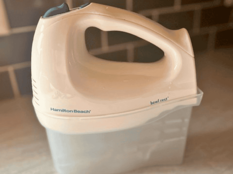 Hamilton Beach hand mixer with beaters resting on a kitchen counter, ready to mix ingredients for homemade desserts and baked goods.