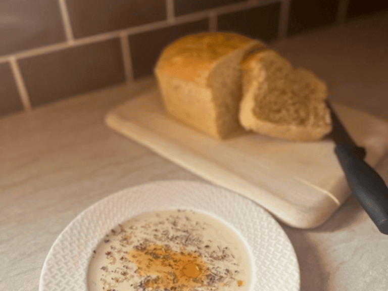 Fresh homemade Italian bread on a wooden cutting board with one sliced piece served beside a small plate of Italian herb dipping oil.