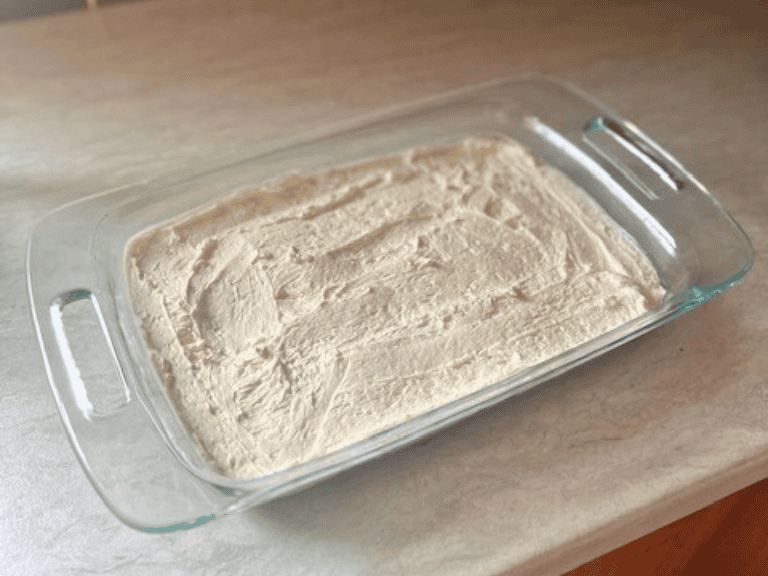 Creamy cheesecake layer spread evenly over the baked pretzel crust in a glass casserole dish for Strawberry Pretzel Salad.