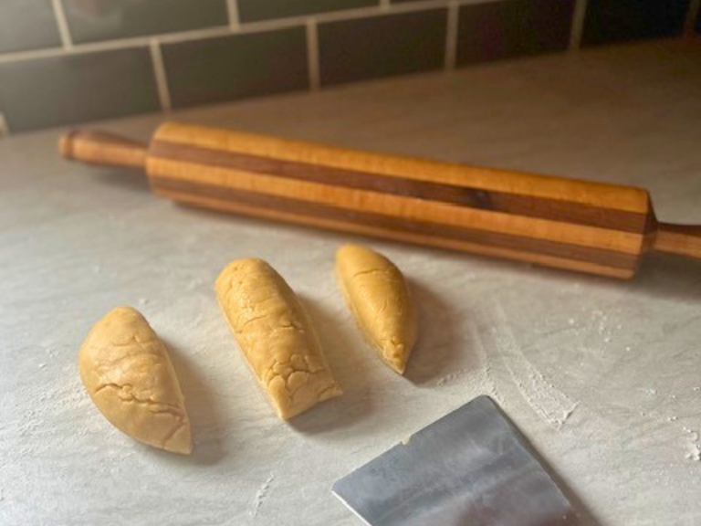 Three portions of homemade pasta dough with a scraper and rolling pin on the counter.