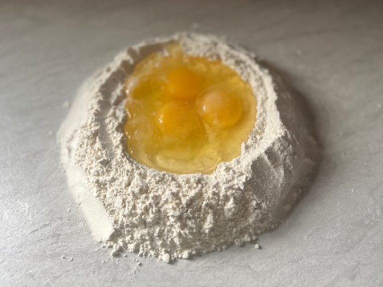 Three large eggs in a well of flour on the countertop for homemade fettuccine dough.