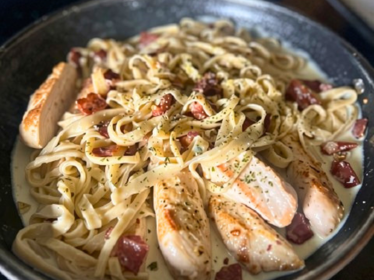 Homemade fettuccine pasta with tender chicken pieces cooking together in a skillet.