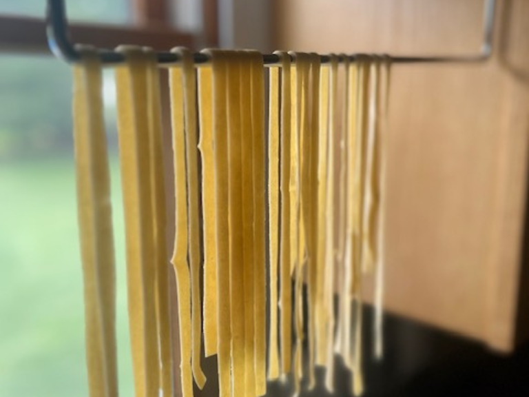 Fresh homemade fettuccine noodles hanging on a drying rack in the kitchen.