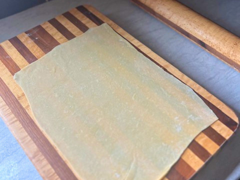 Homemade pasta dough rolled into a rectangle on a cutting board.